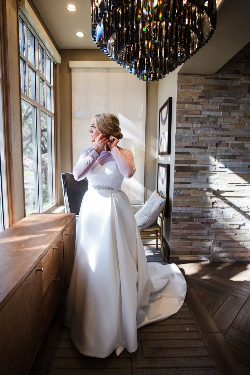 Bride wearing a Robert bullock Wedding Gown puts on her earrings at stone briar country club