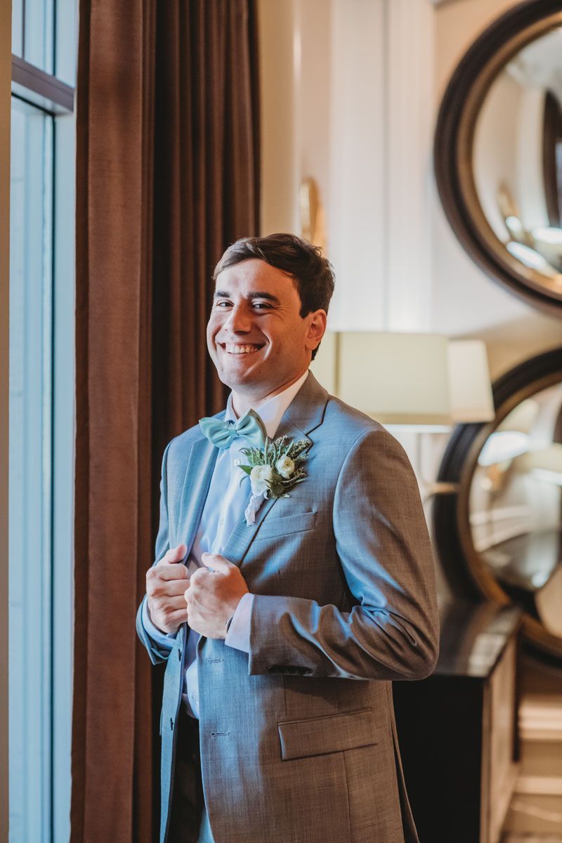 Groom in a gray tuxedo poses in front a window in Frisco Texas