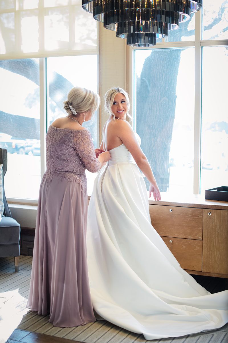 Mom in Lilac Lace Dress buttons her daughter into her Robersons bullock bridal gown