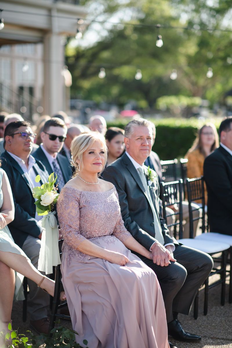 Mother of the bride wearing Lilac lace grown holds hands with husband wearing gray suit during wedding at Stone Briar CC