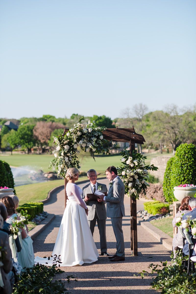 A bride wearing a Robert Bullock wedding gown exchanges wedding rings with groom wearing a grey tuxedo at Stone Briar
