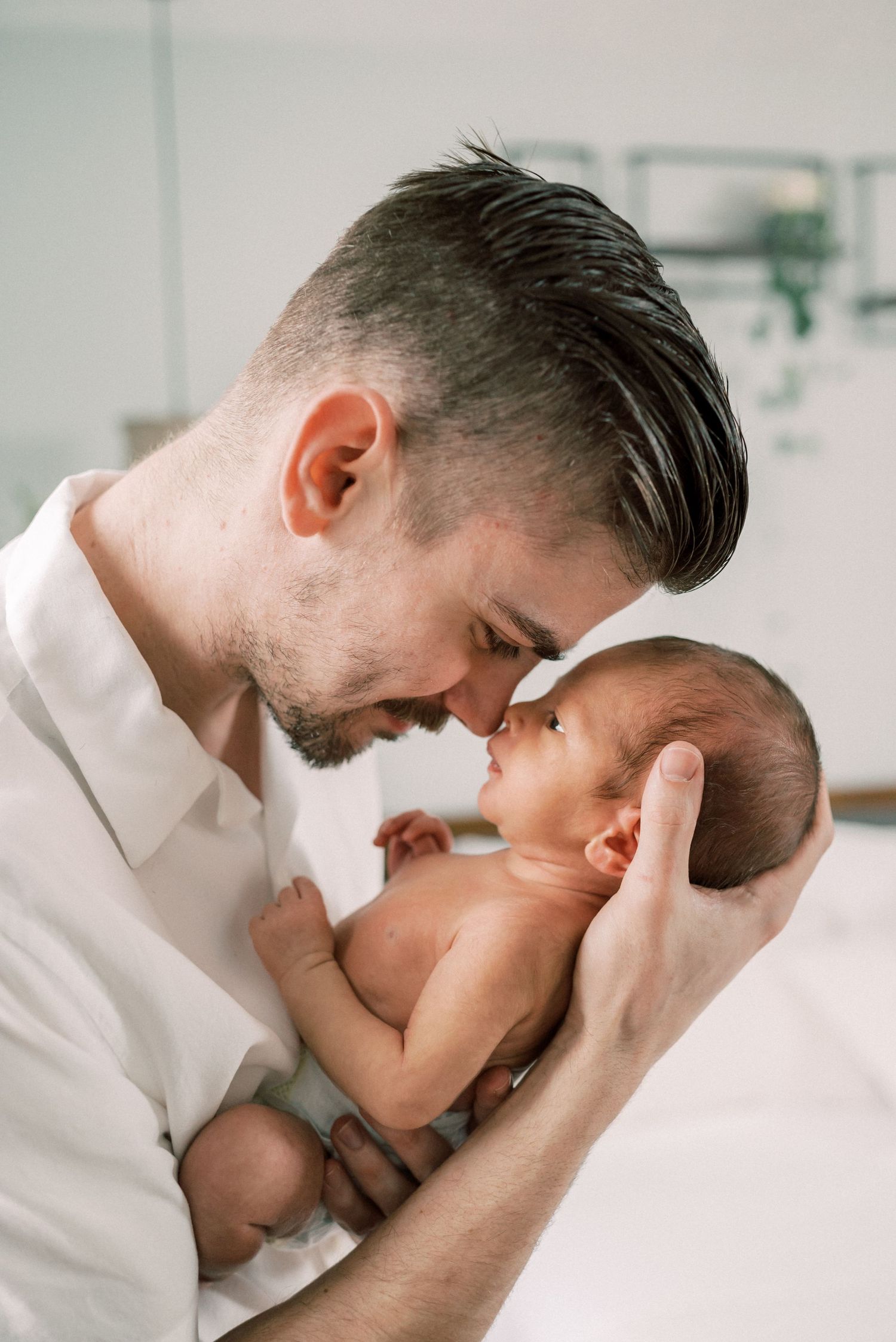 Parent tenderly holding and nuzzling newborn baby in white room.