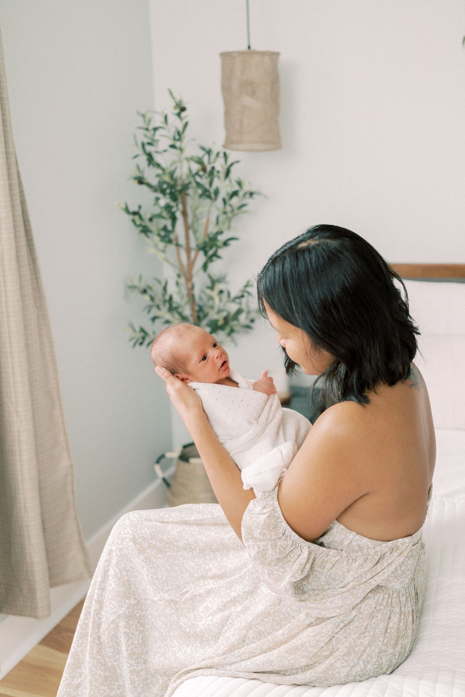 Parent and infant share an intimate moment in a bright bedroom with greenery.
