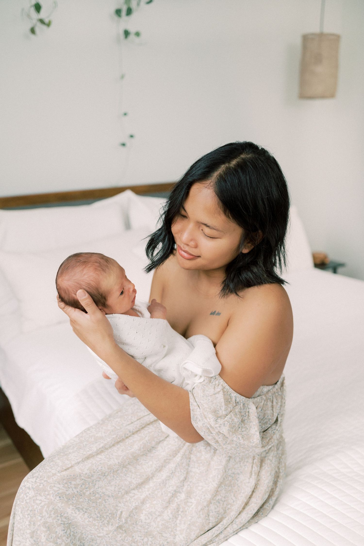 Parent in white dress lovingly cradling newborn on white bed.