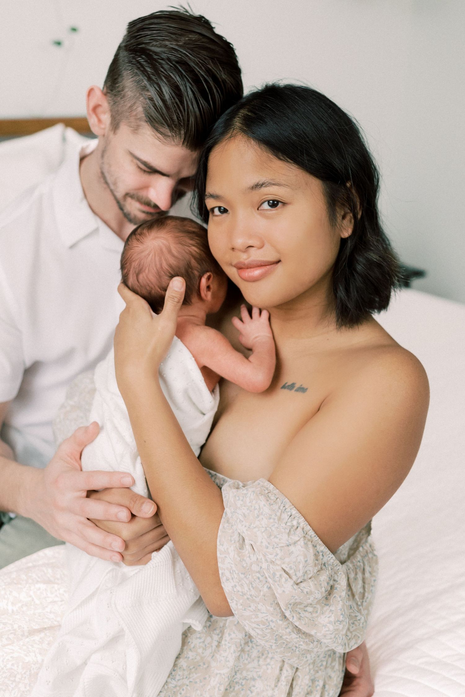 Parents snuggling with their newborn baby on white bedding.