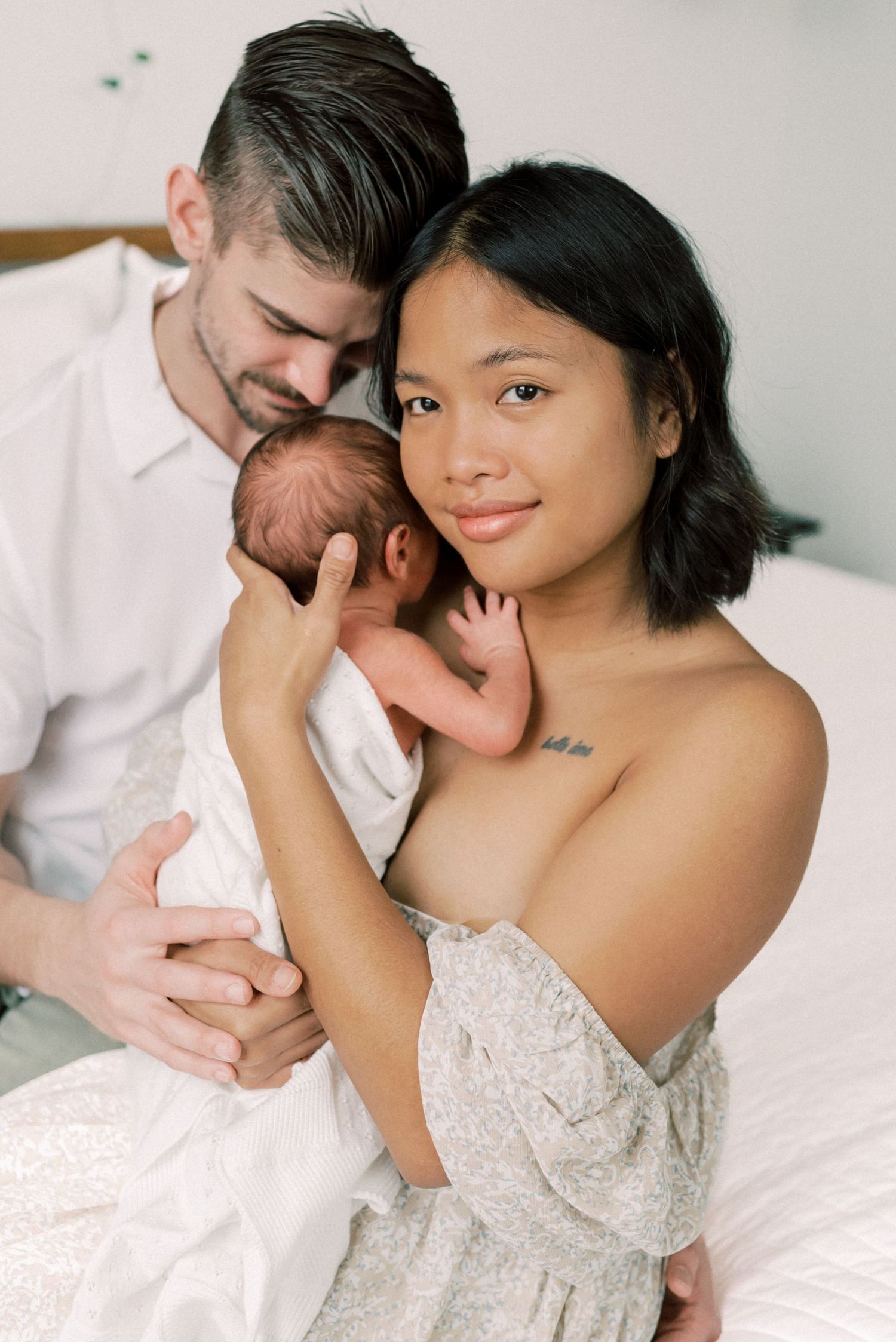 A newborn baby being cradled in white clothing against a neutral background.