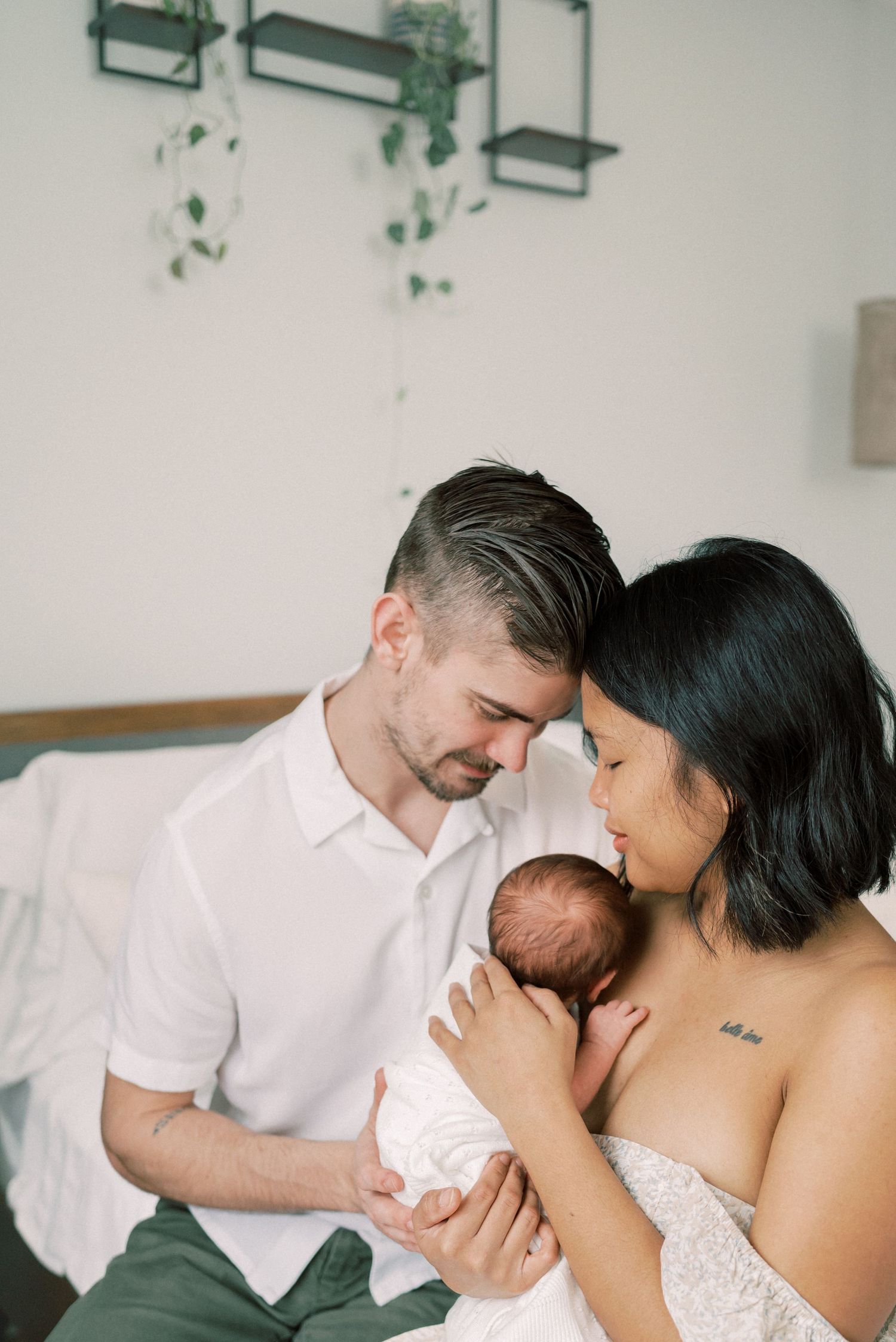 A gentle family moment against white walls with hanging plants in the background.