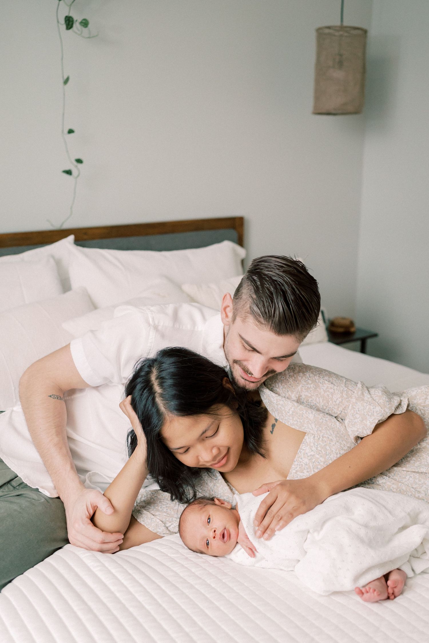 Intimate family moment captured on white bedding with vine decor on wall.