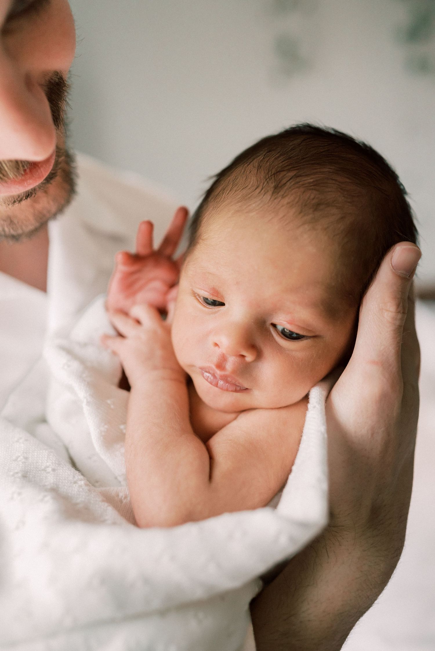Newborn wrapped in white blanket with gentle support.