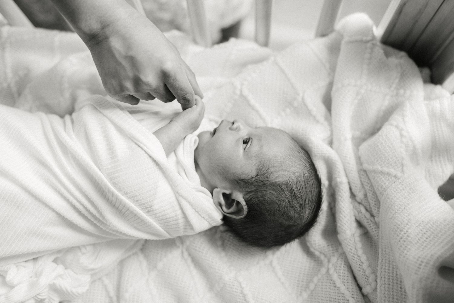 A black and white portrait of a newborn baby wrapped in white linens.