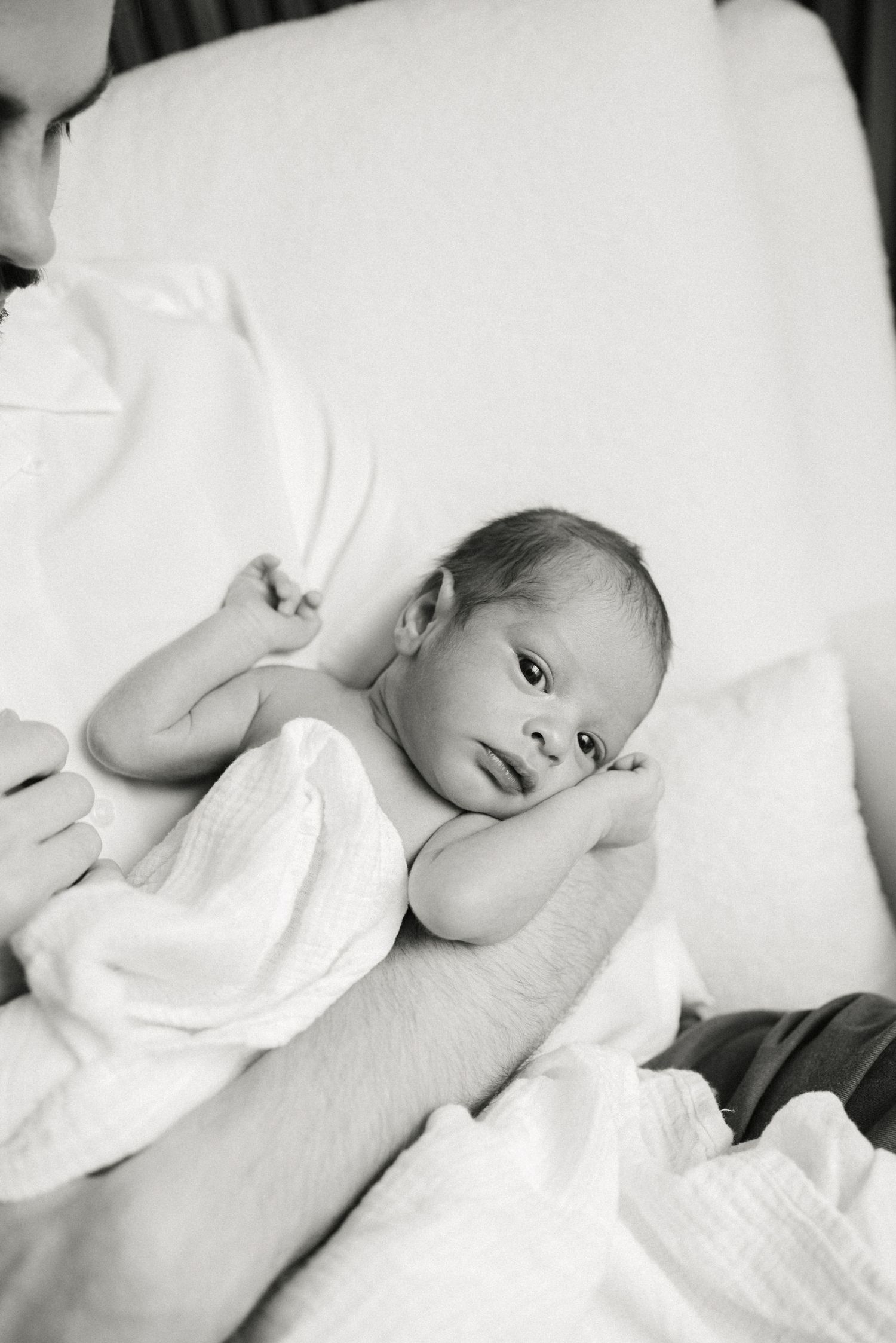 A black and white image of a baby resting on soft white fabric.