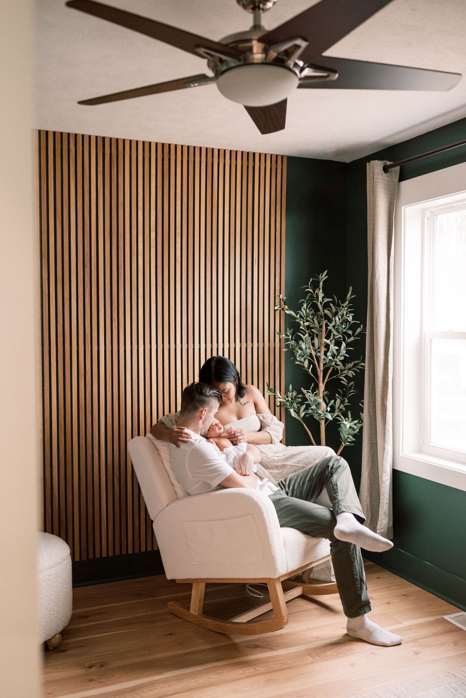 A modern nursery with wood slat accent wall, rocking chair, and ceiling fan.