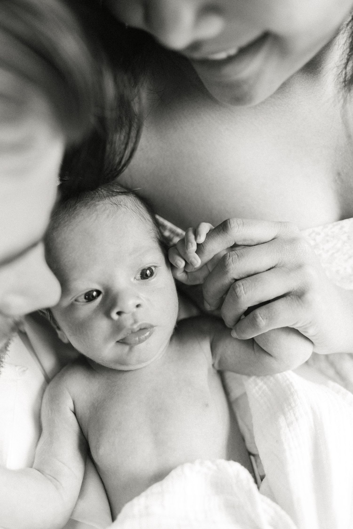 A black and white close-up portrait of a newborn baby against white fabric.