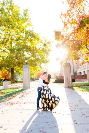 woman in black and gold skirt hugging and kissing man in white shirt at Purdue University in the fall at sunset