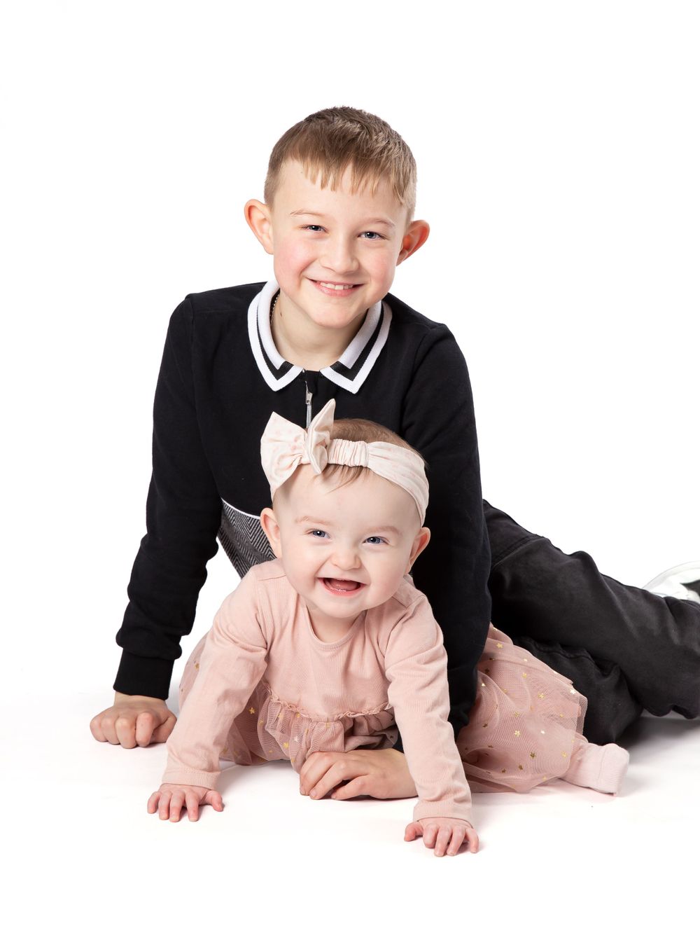 boy holding baby girl in pink dress sat on white background