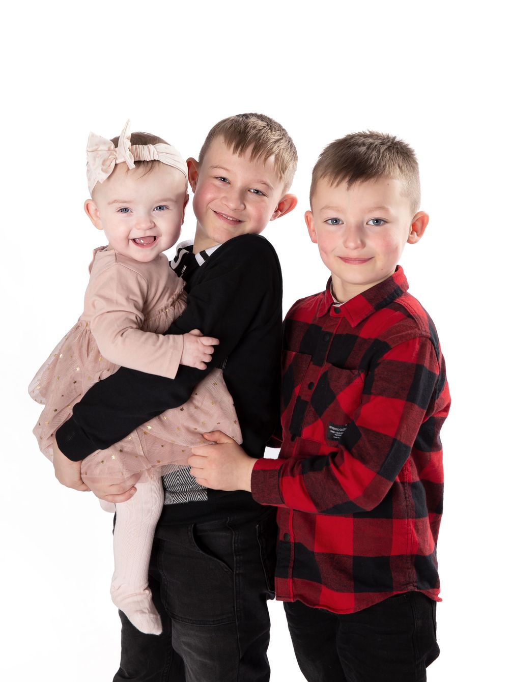 2 boys one in red check shirt other in navy jumper who is holding a baby girl in a pink dress