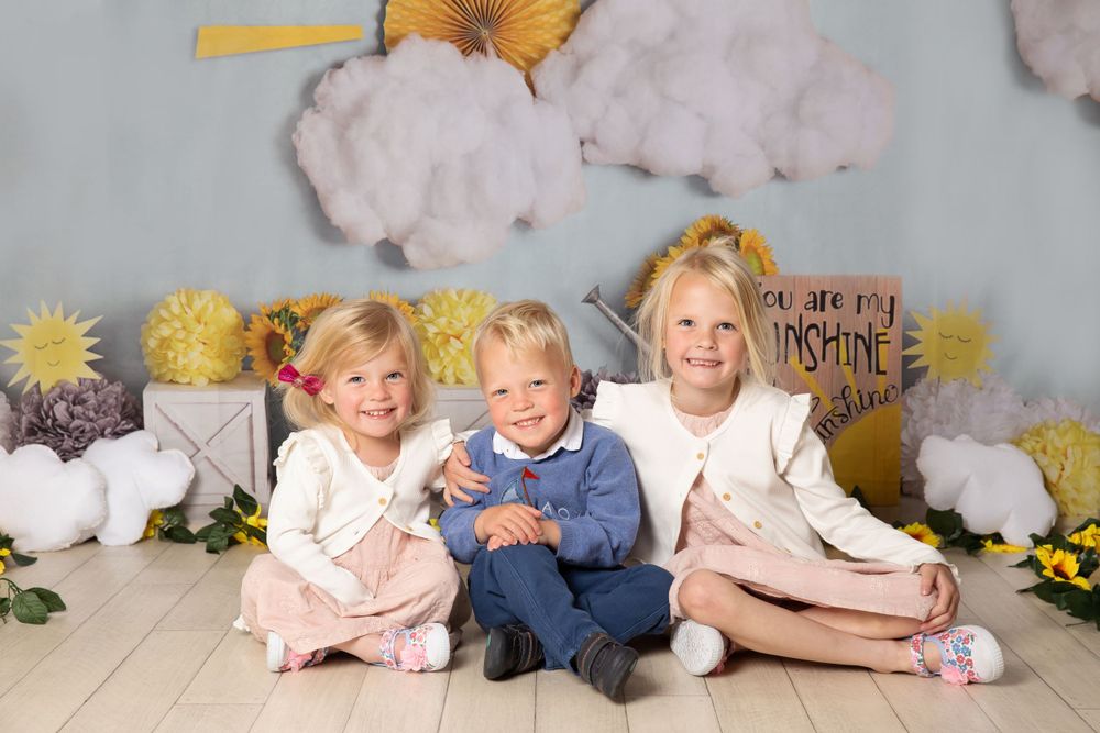 3 small children 2 girls and 1 boy in the middle with a sunshine background
