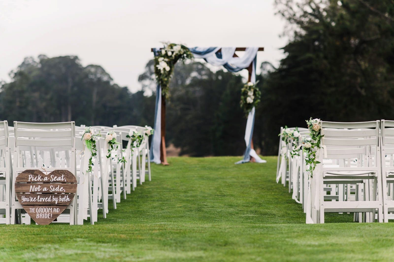 Ceremony site with white chairs. Beautiful wedding arch with blue and white fabric. White floral details.