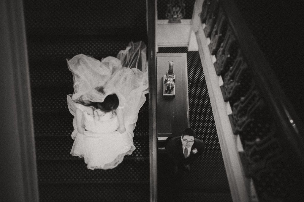 Bride and groom walking down elegant hotel staircase in wedding attire | Calgary wedding photographer capturing timeless, romantic moments.