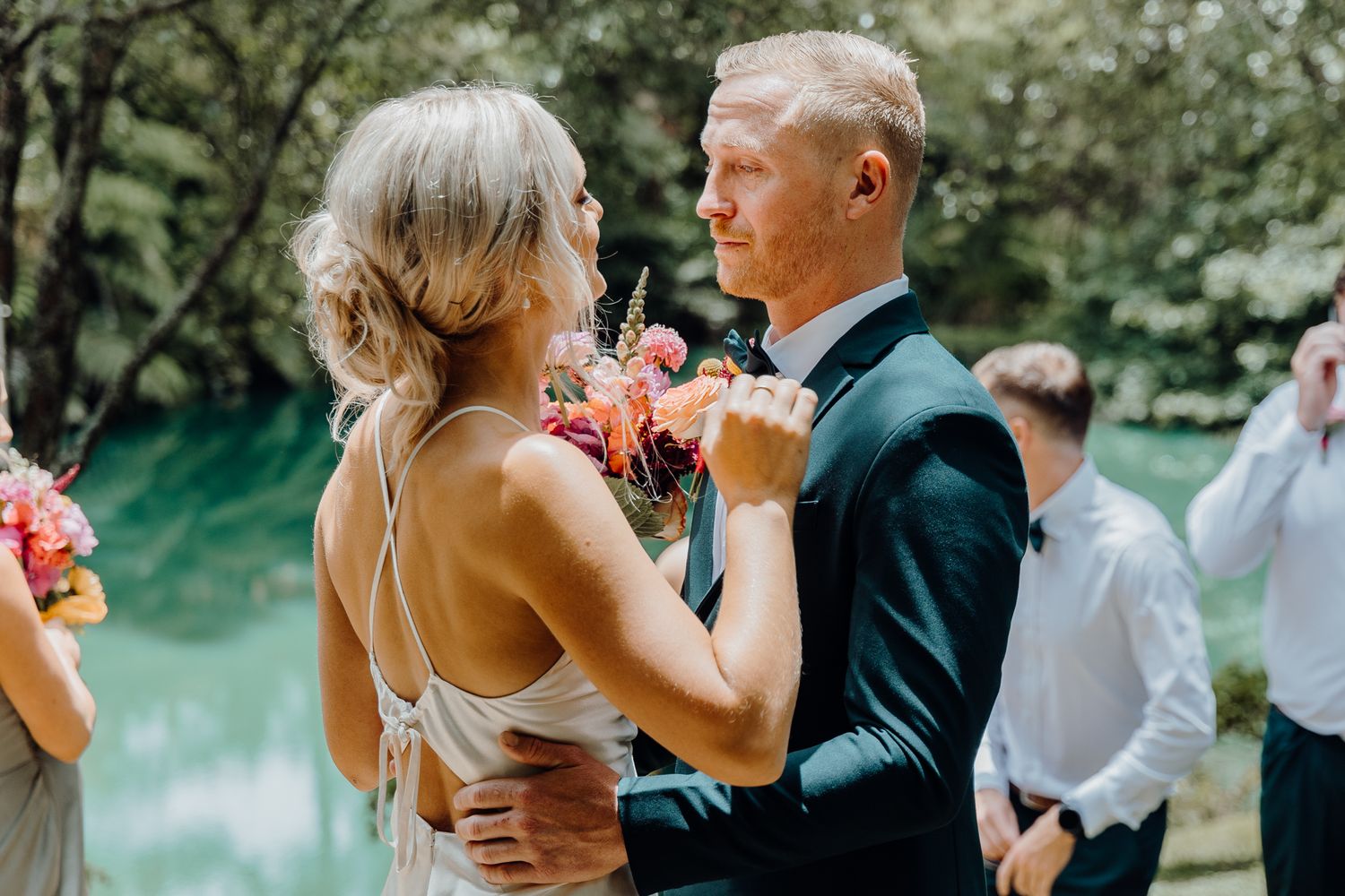 Elegant couple dances together during outdoor wedding celebration beside a serene lake.