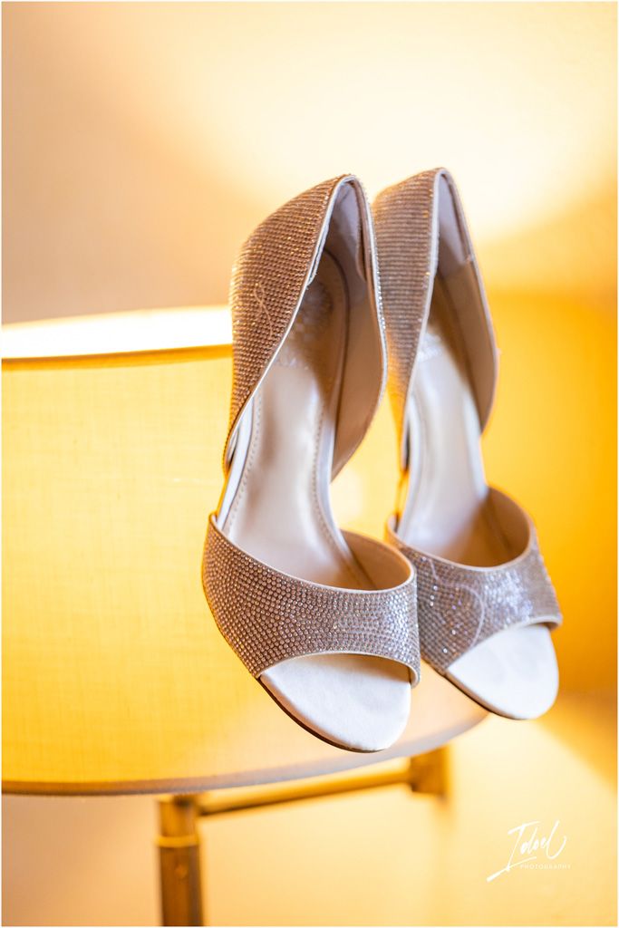 Elegant sparkly bridal shoes with peep toe design photographed on golden surface.