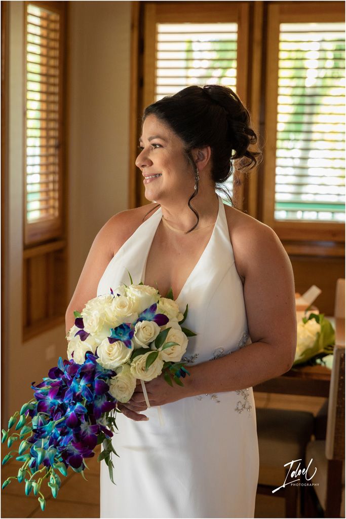 A bride in a white halter dress smiles while holding a cascading blue and white bouquet.