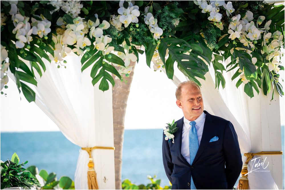 A tropical wedding scene with white orchids and monstera leaves framing an ocean backdrop.