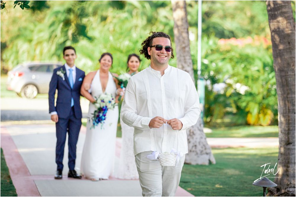 Wedding party members walk along a garden path with palm trees in the background.