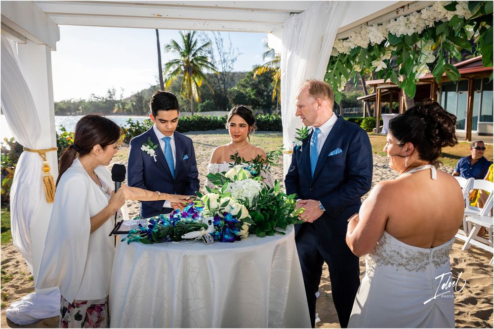 Wedding party gathered around signing table during beach ceremony with tropical decor.