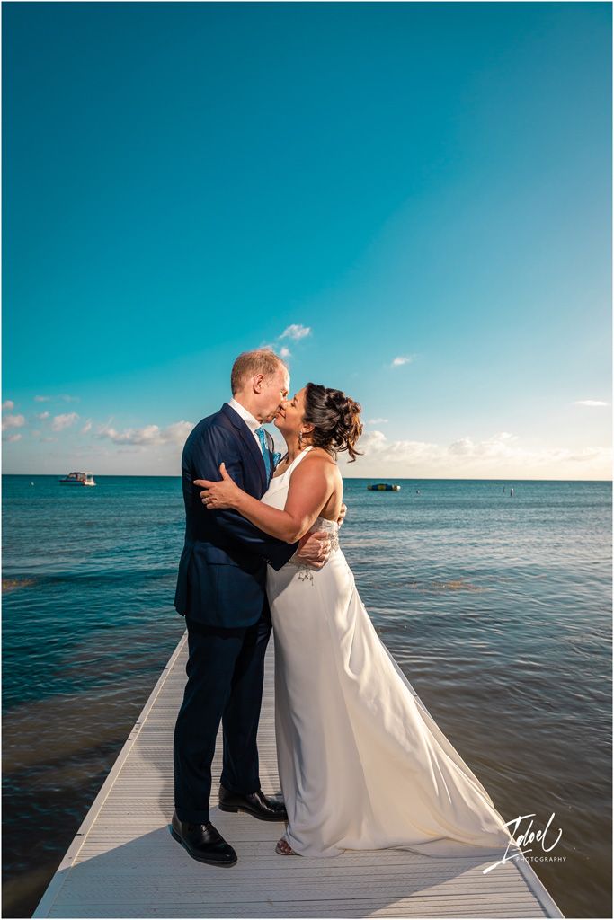 A romantic moment captured on a waterfront dock with turquoise ocean waters in the background.