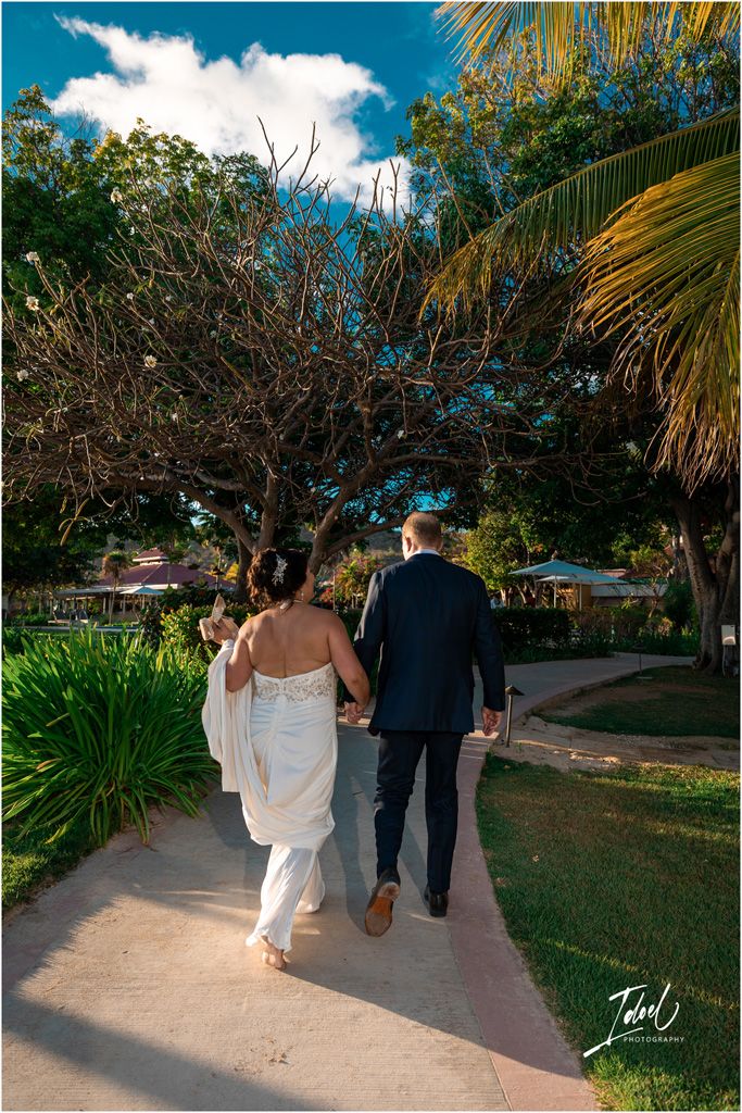 A couple walking along a tropical garden path lined with palm trees and lush foliage.