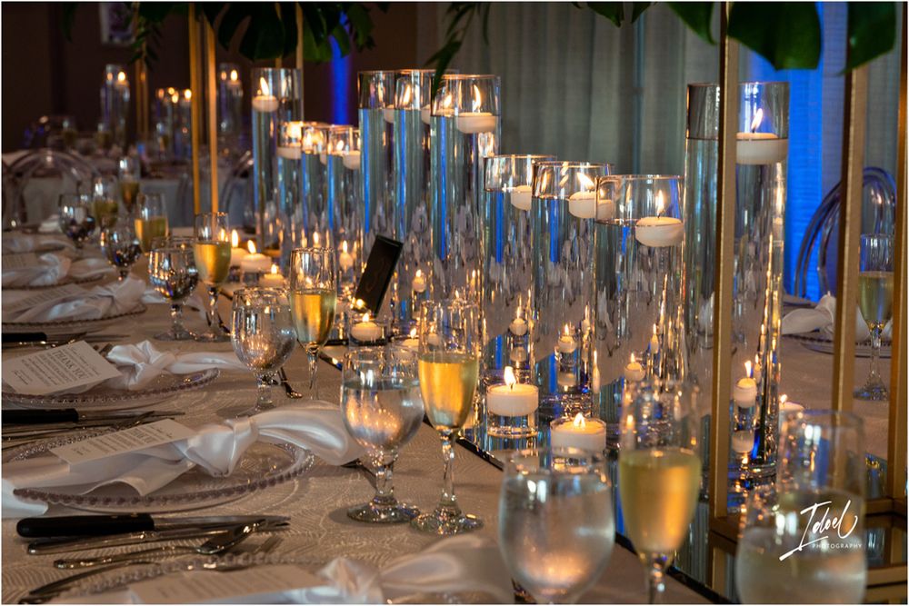 Romantic candlelit wedding reception table with glass hurricanes and elegant place settings.