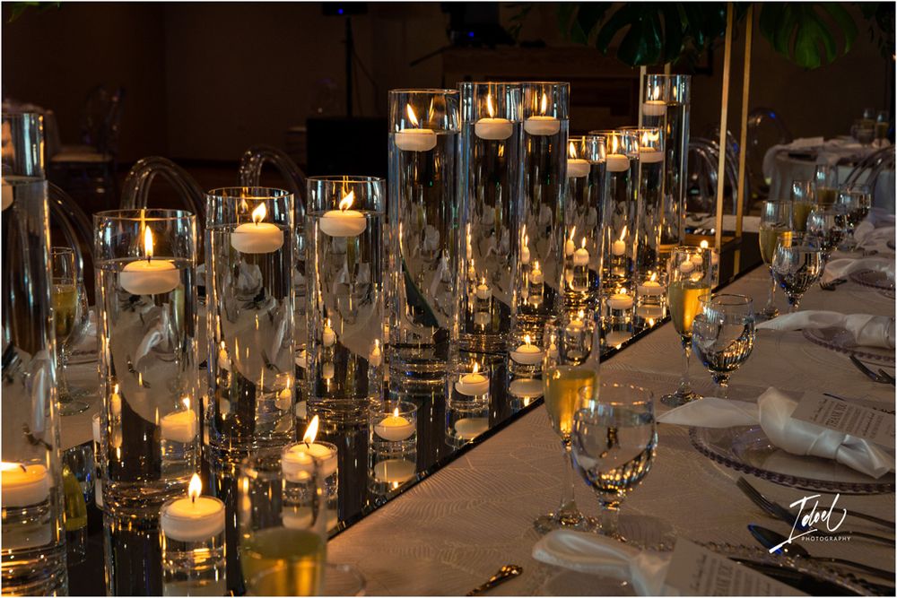 Elegant table setting with glass cylinders holding lit candles creating romantic ambiance at a wedding reception.