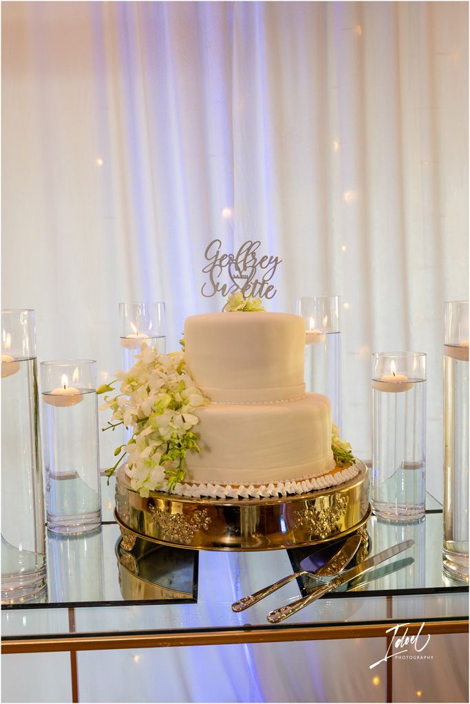 Classic white two-tier wedding cake displayed on a mirrored stand with floating candles and soft lighting.