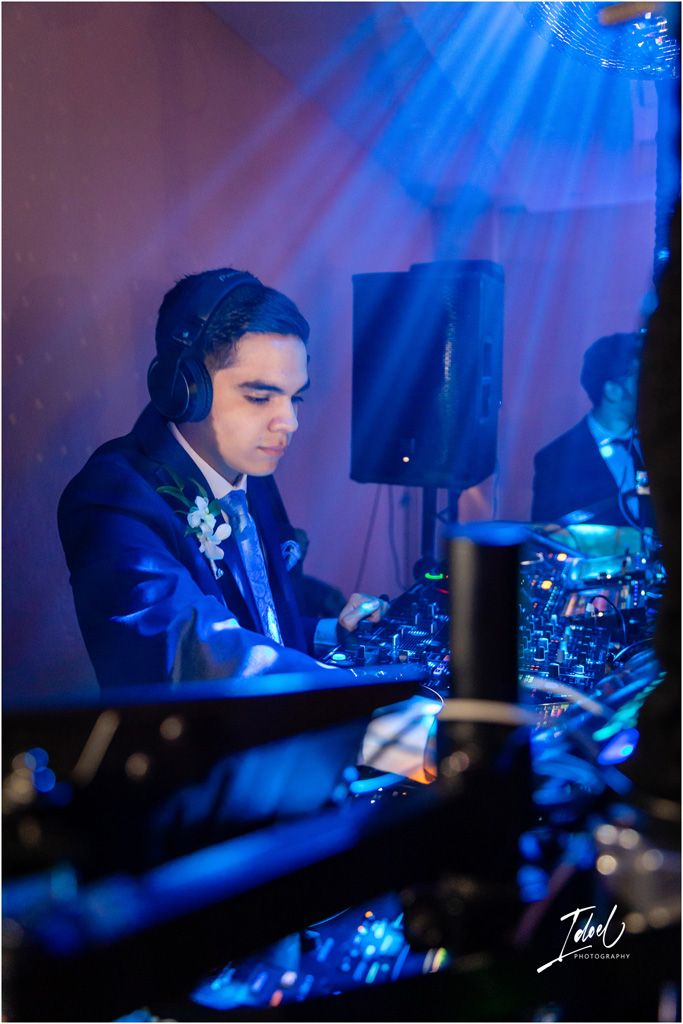DJ in blue suit mixing music at wedding reception under dramatic blue lighting.