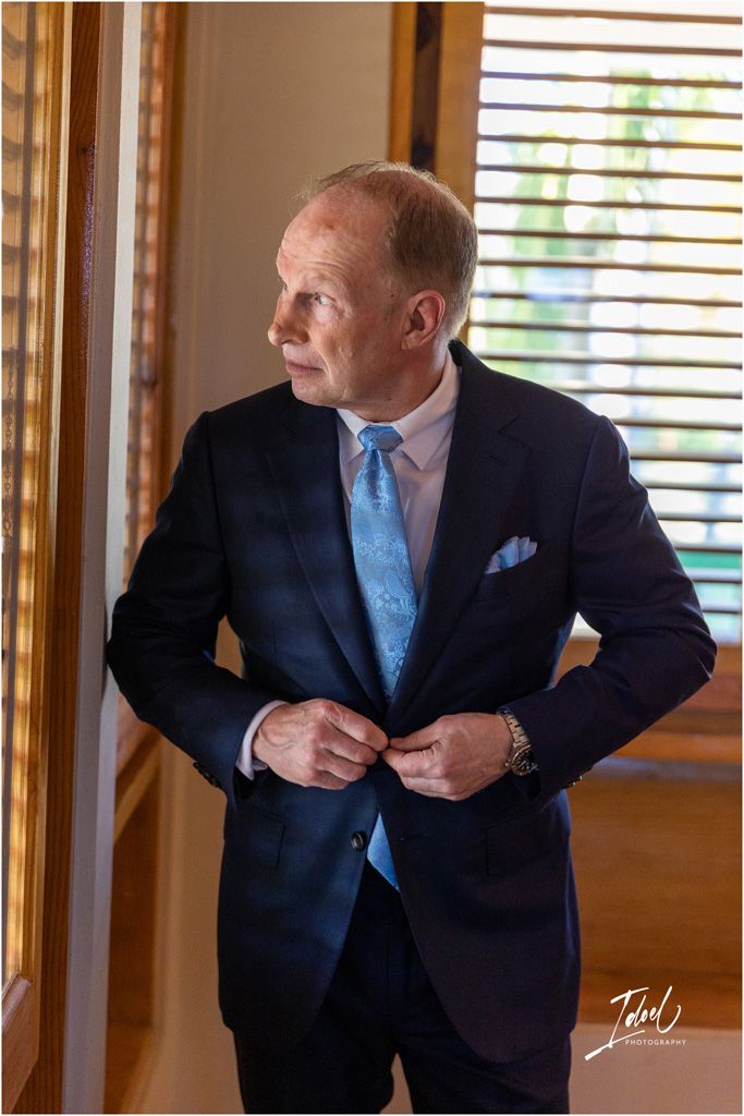 A formal portrait shows someone adjusting their navy suit jacket with a light blue tie.