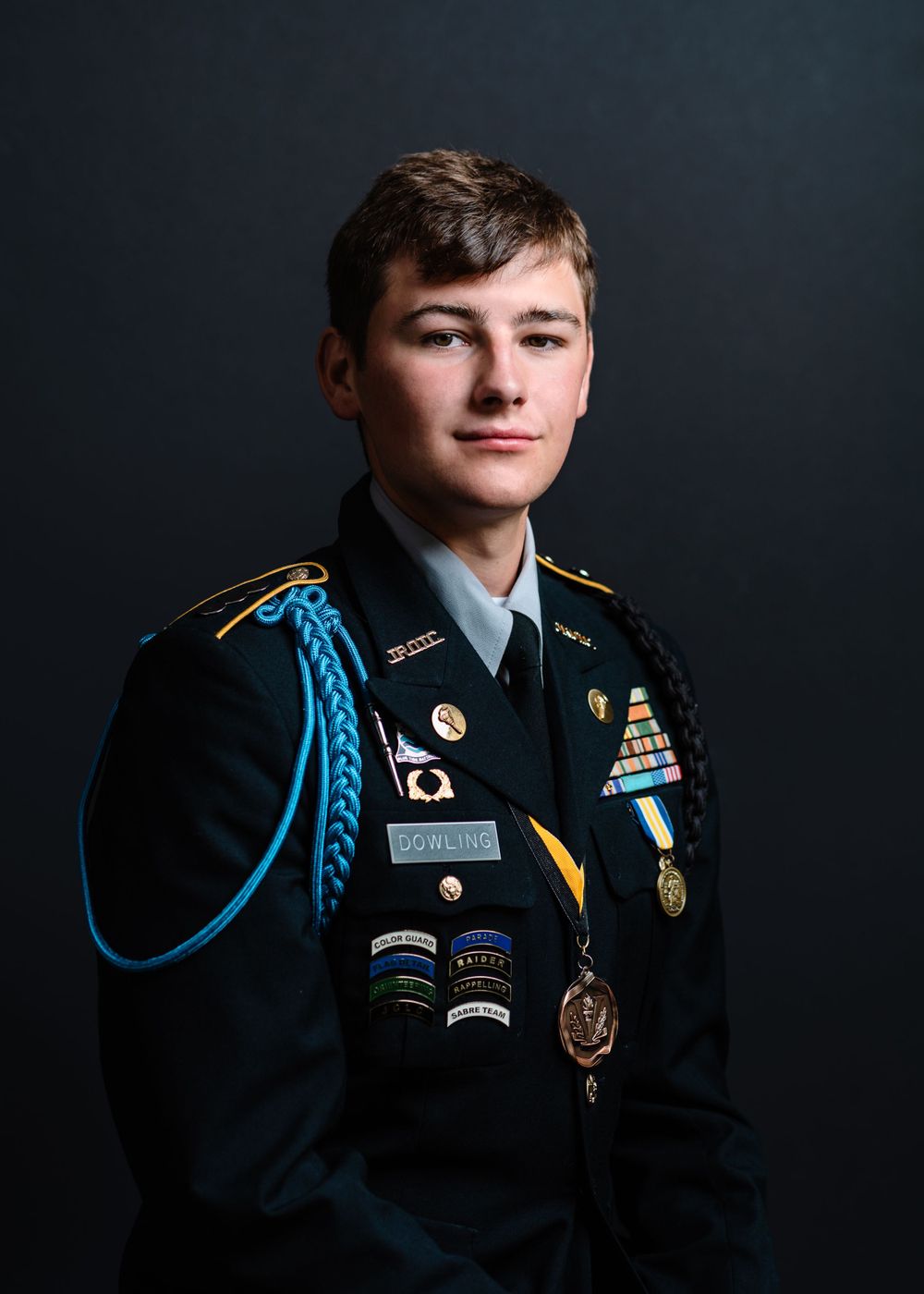Military portrait in dress uniform with decorations and blue cord against dark background.
