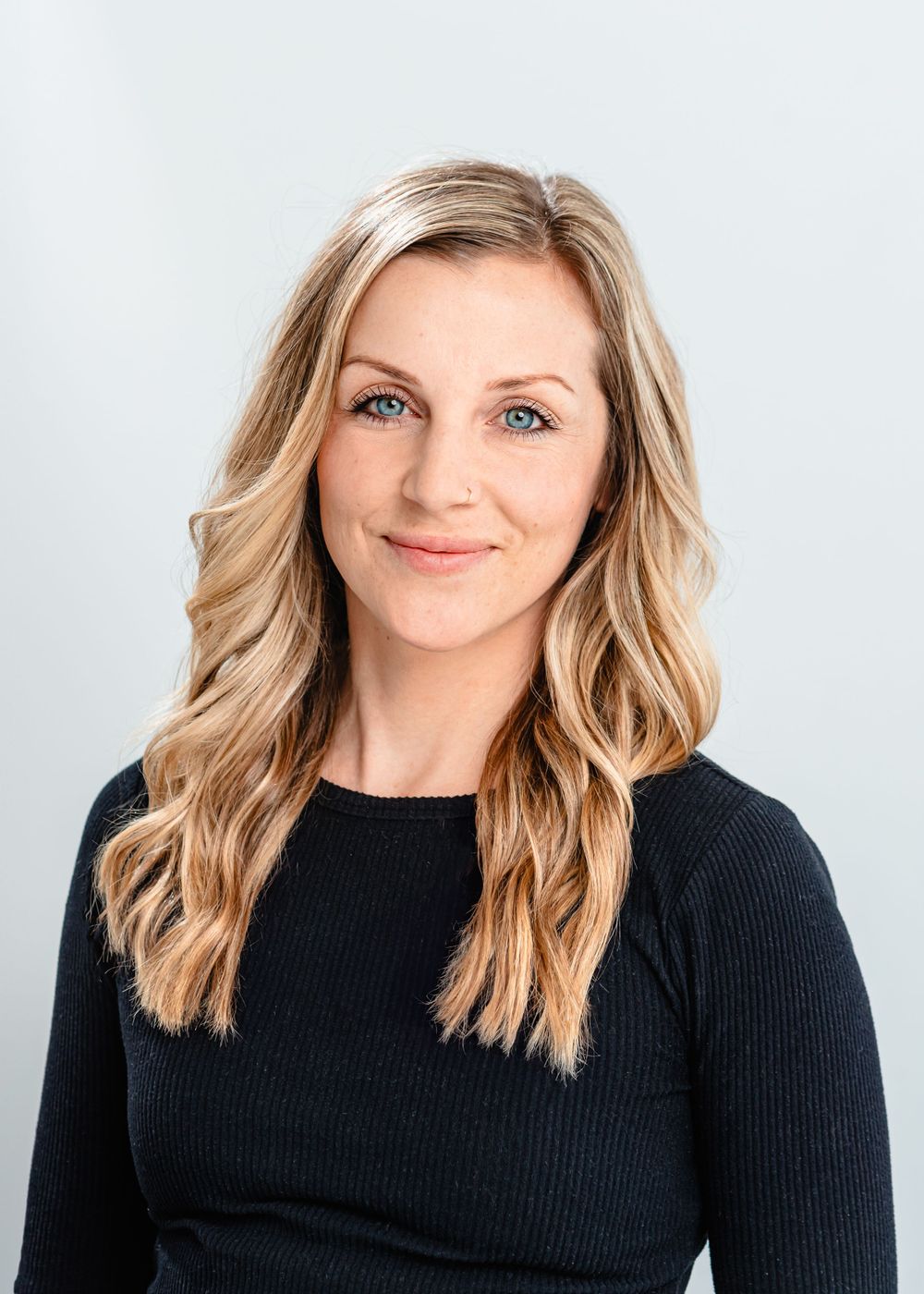 Professional headshot with wavy blonde hair wearing black sweater against light background.