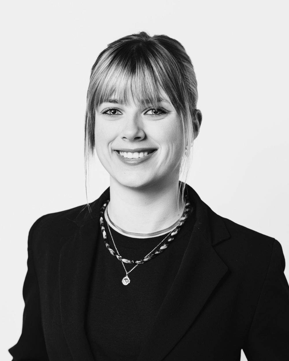 Professional black and white studio portrait with layered necklaces and blazer.