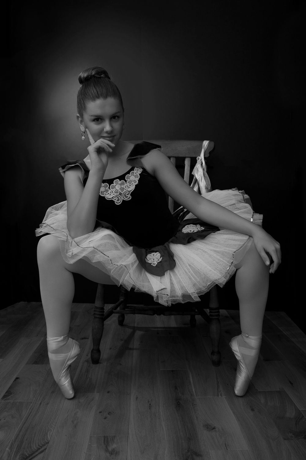black and white image of ballerina wearing tutu, sat on chair.