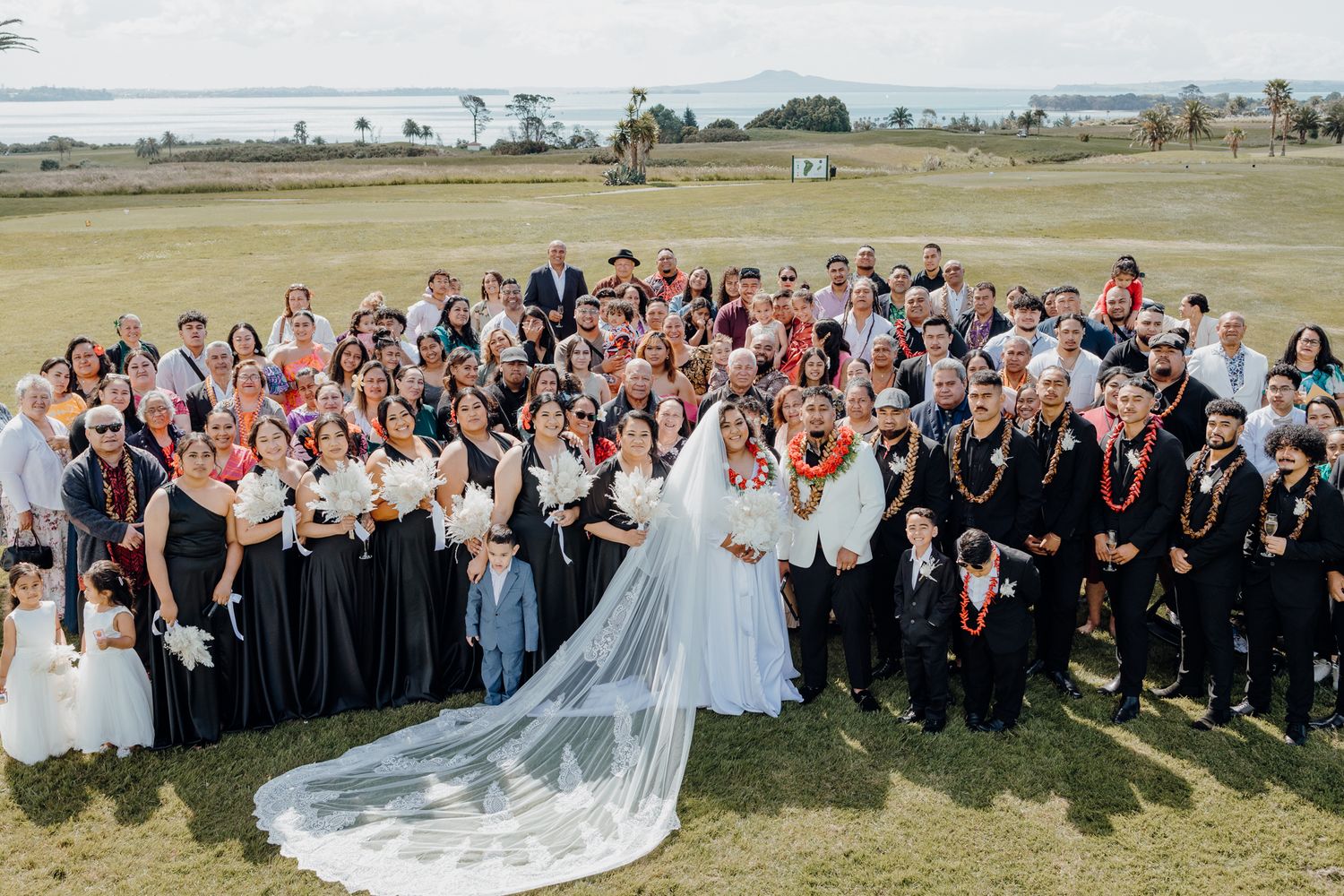 Large group photo of wedding party and guests on a grassy oceanfront lawn.