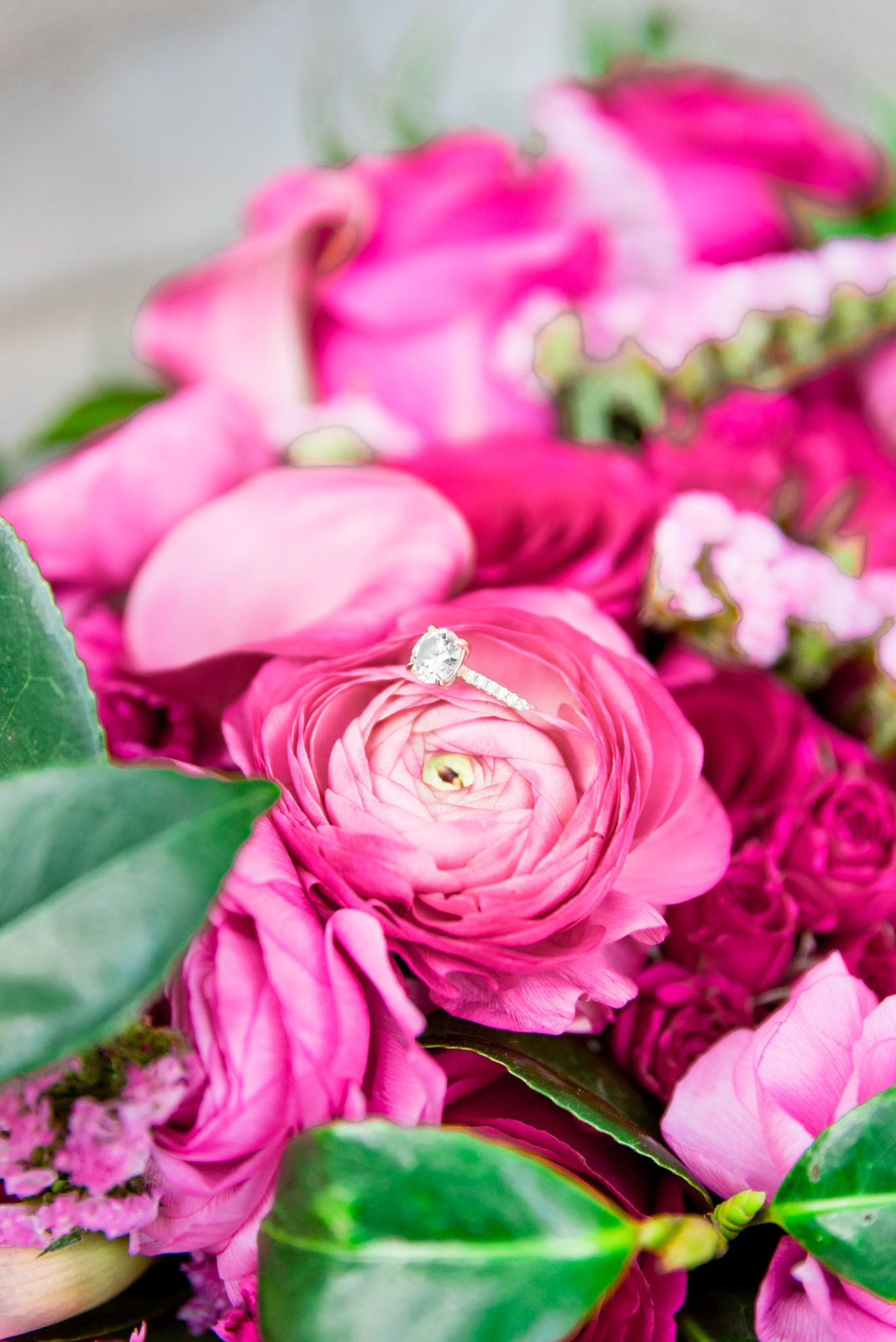 diamond engagement ring sitting in bouquet of pink ranunculus and greenery
