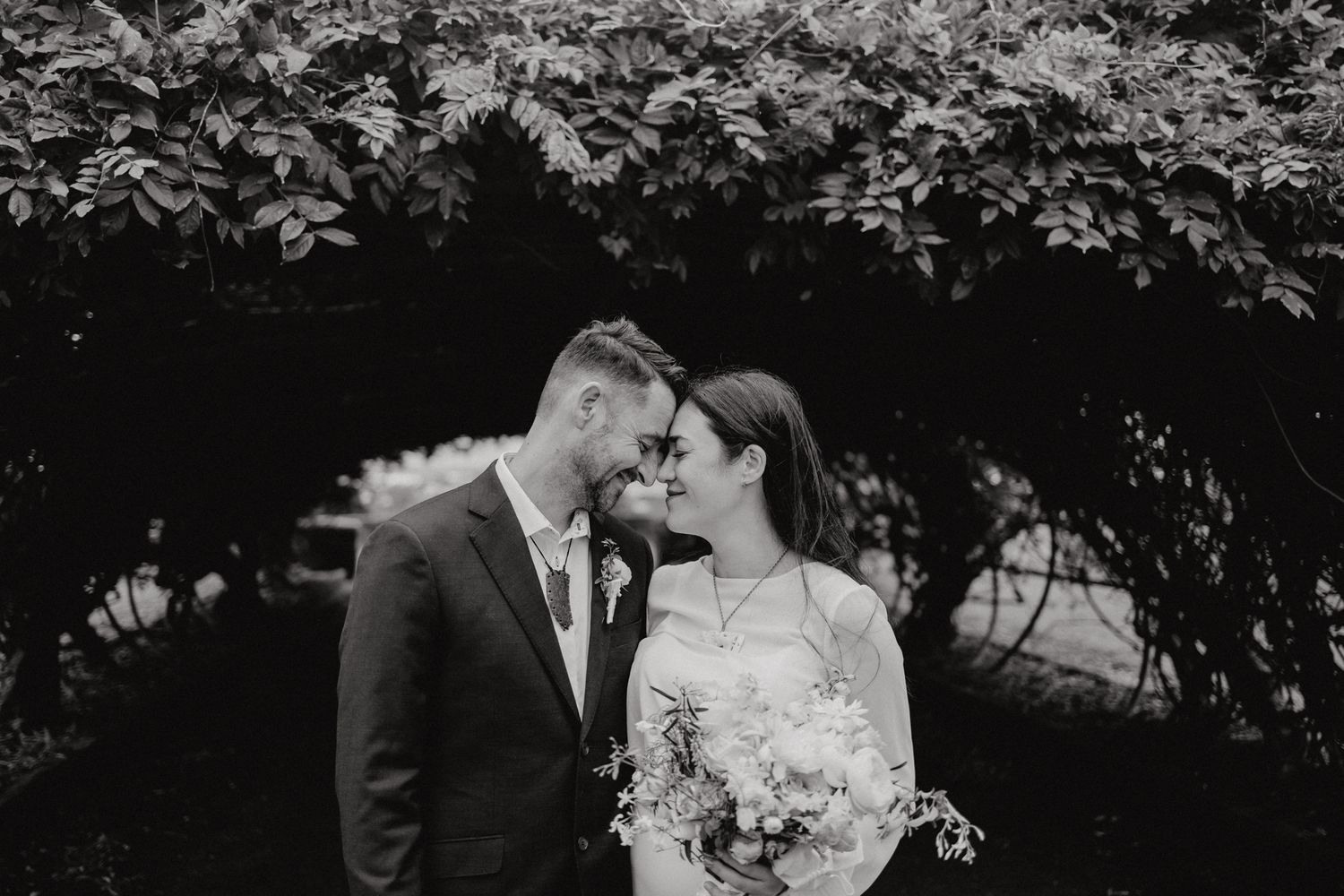 A romantic black and white portrait of a couple against lush garden foliage.