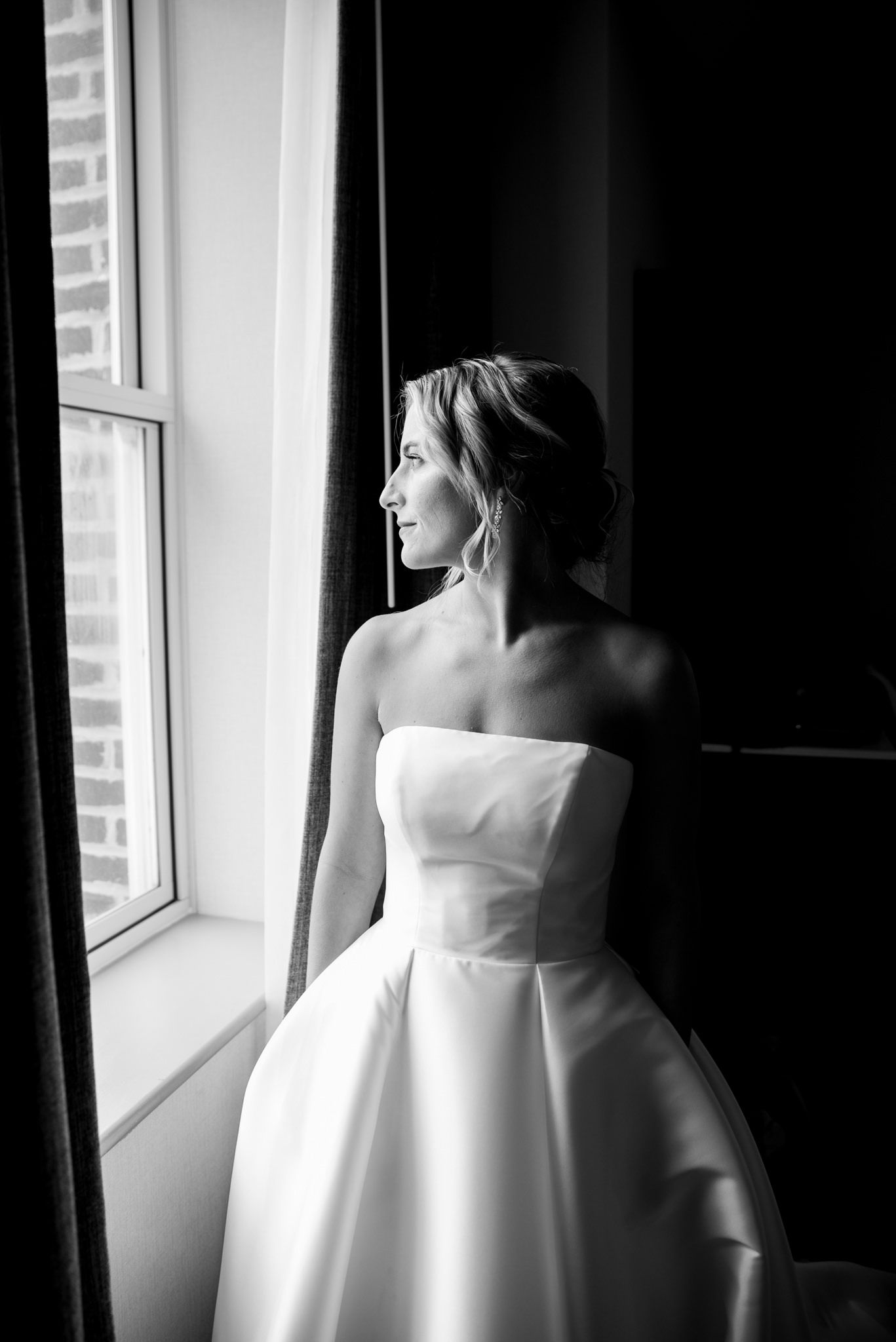 blonde bride with updo and strapless wedding dress looking out the window while getting ready