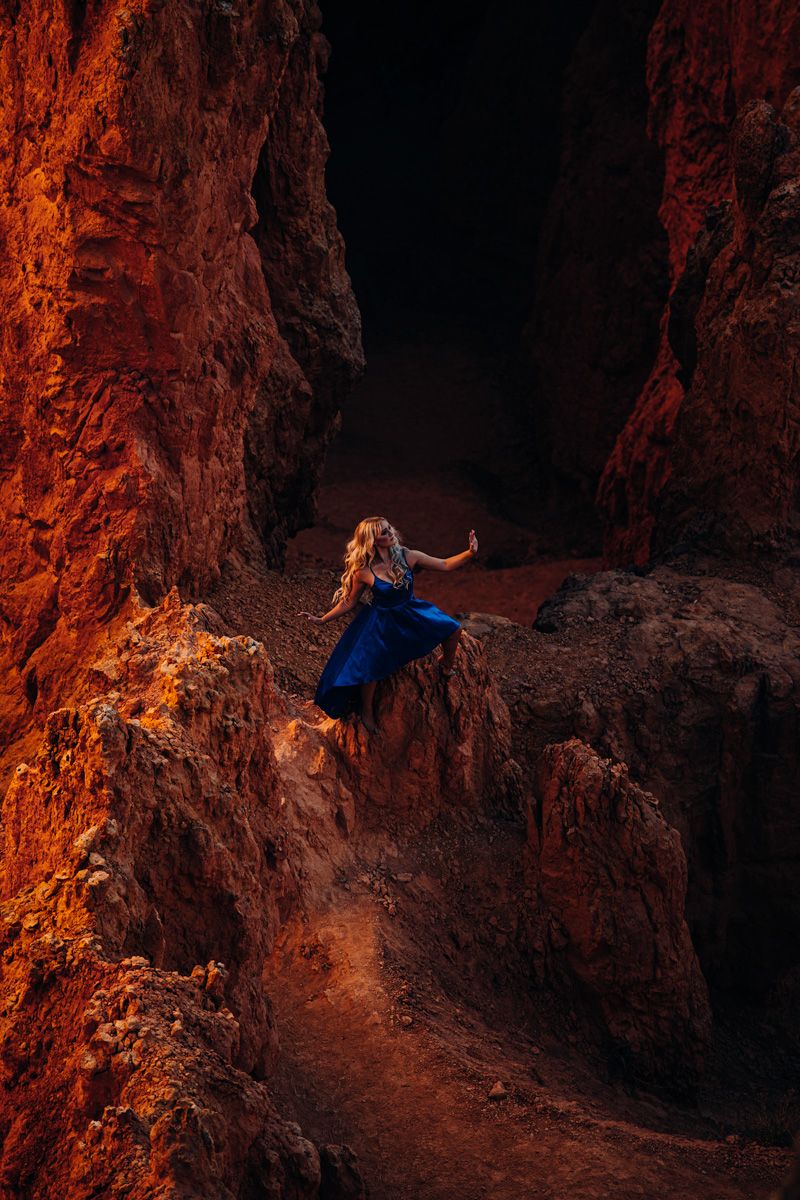 woman in a blue dress posing hopefully in a menacing red rock slot canyon cliff