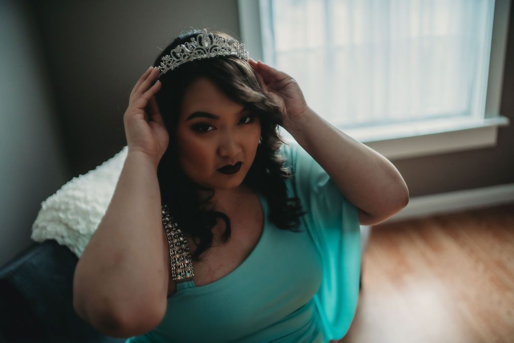 boudoir image of a woman straightening her crown, looking directly into the camera, locking eyes with the viewer