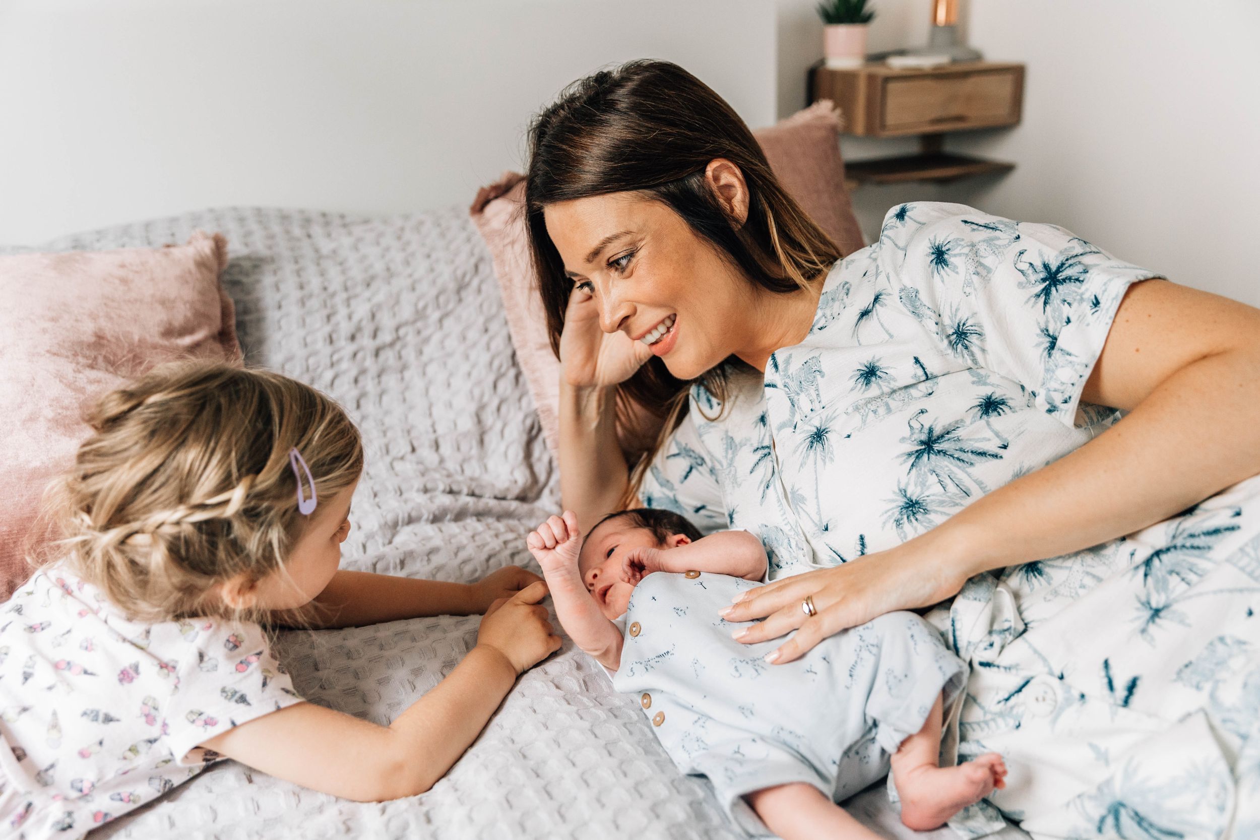 mum and toddler girl cuddling with baby brother on bed
