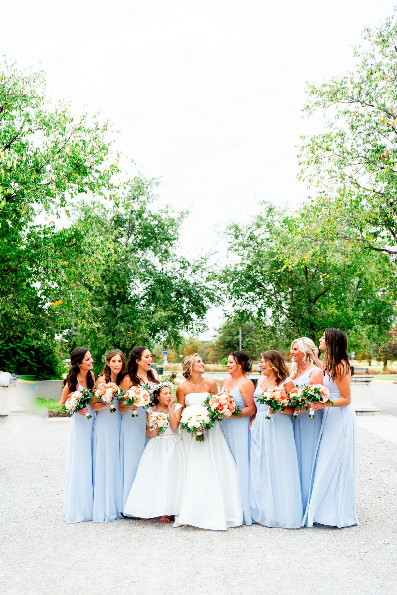 bride laughs with bridesmaids in light blue dresses and coral bouquets at STL Forest Park fall wedding