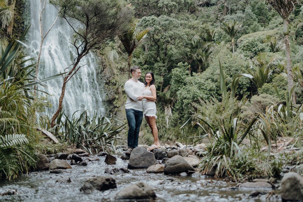 A romantic moment captured on rocky terrain with a majestic waterfall backdrop.