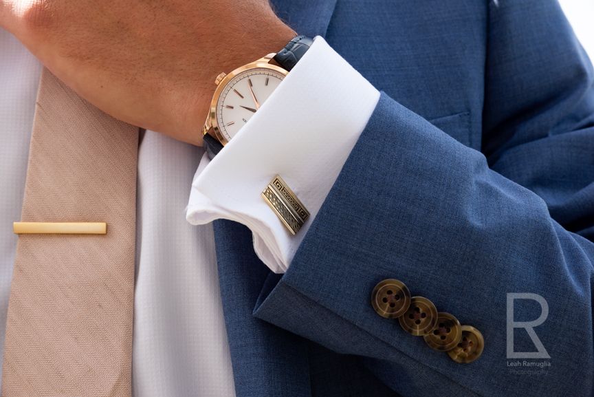 Leah Ramuglia Photography a groom adjust his tie on his blue suite with gold tie clip, watch, and cuff links